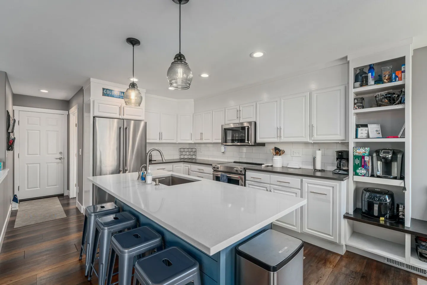 Kitchen with white cabinetry, stainless steel appliances, and a blue island with barstools.