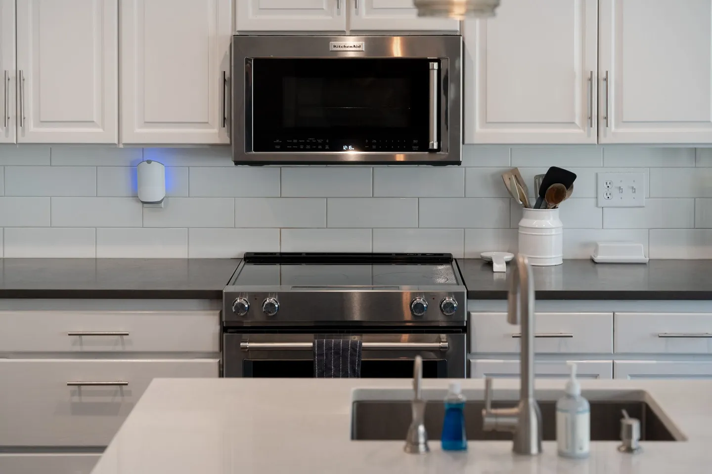 Kitchen counter area with an electric range, stainless steel over-the-range microwave, subway tile backsplash, and foreground sink island.