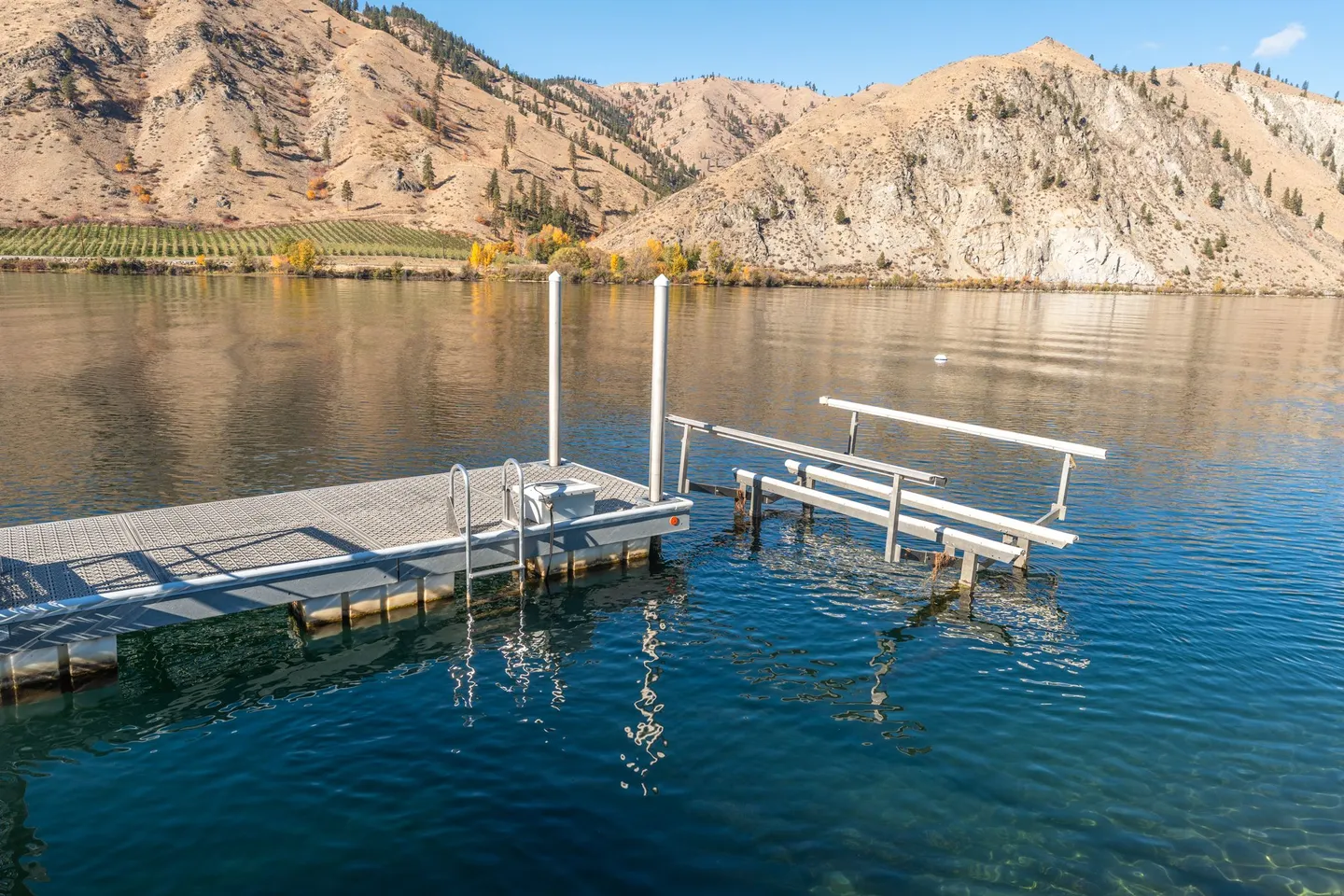 Floating dock and boat lift situated on clear, calm water with arid mountains in the background under a blue sky.