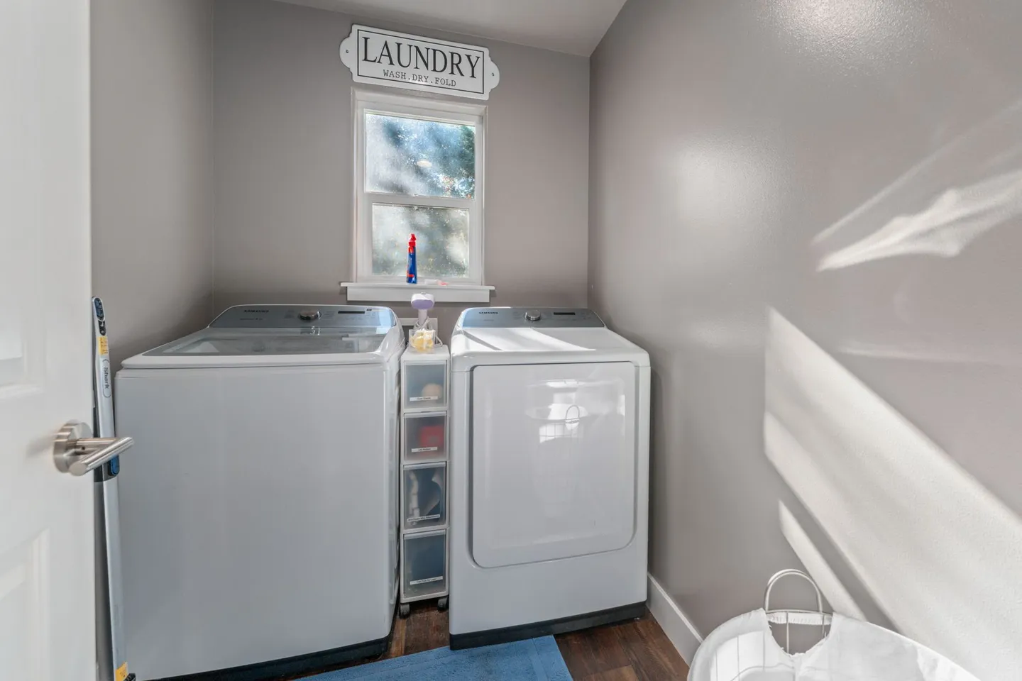 Dedicated indoor laundry room featuring a white washer and dryer with a small window and storage cart between them.