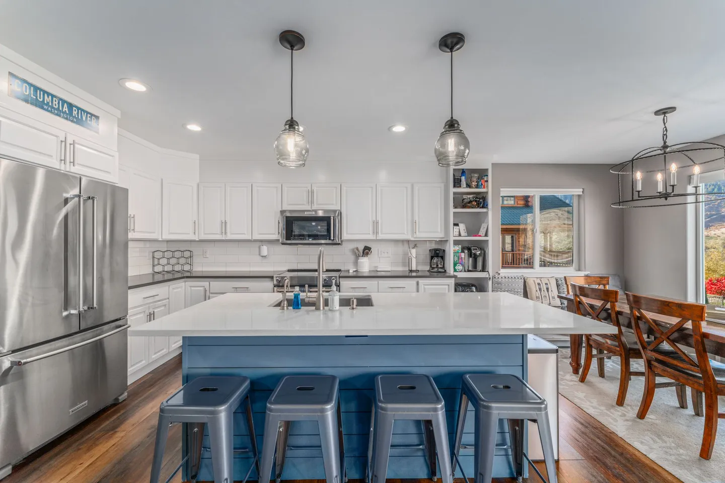 Open kitchen featuring a blue island with four metal stools, white cabinetry, stainless steel appliances, and an adjacent dining area.