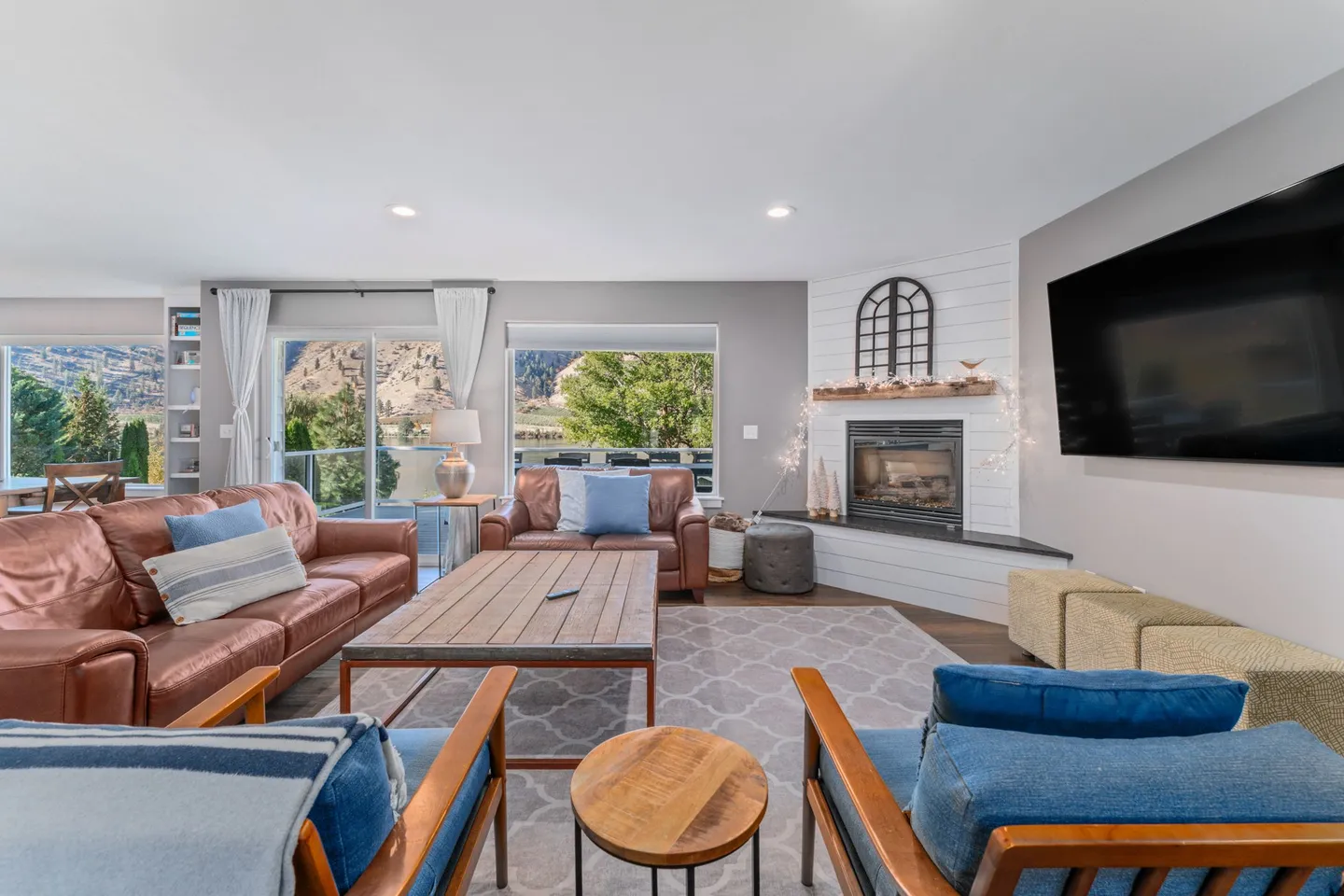 Living room with brown leather sofas, blue armchairs, a fireplace, and large windows showing a mountain view.