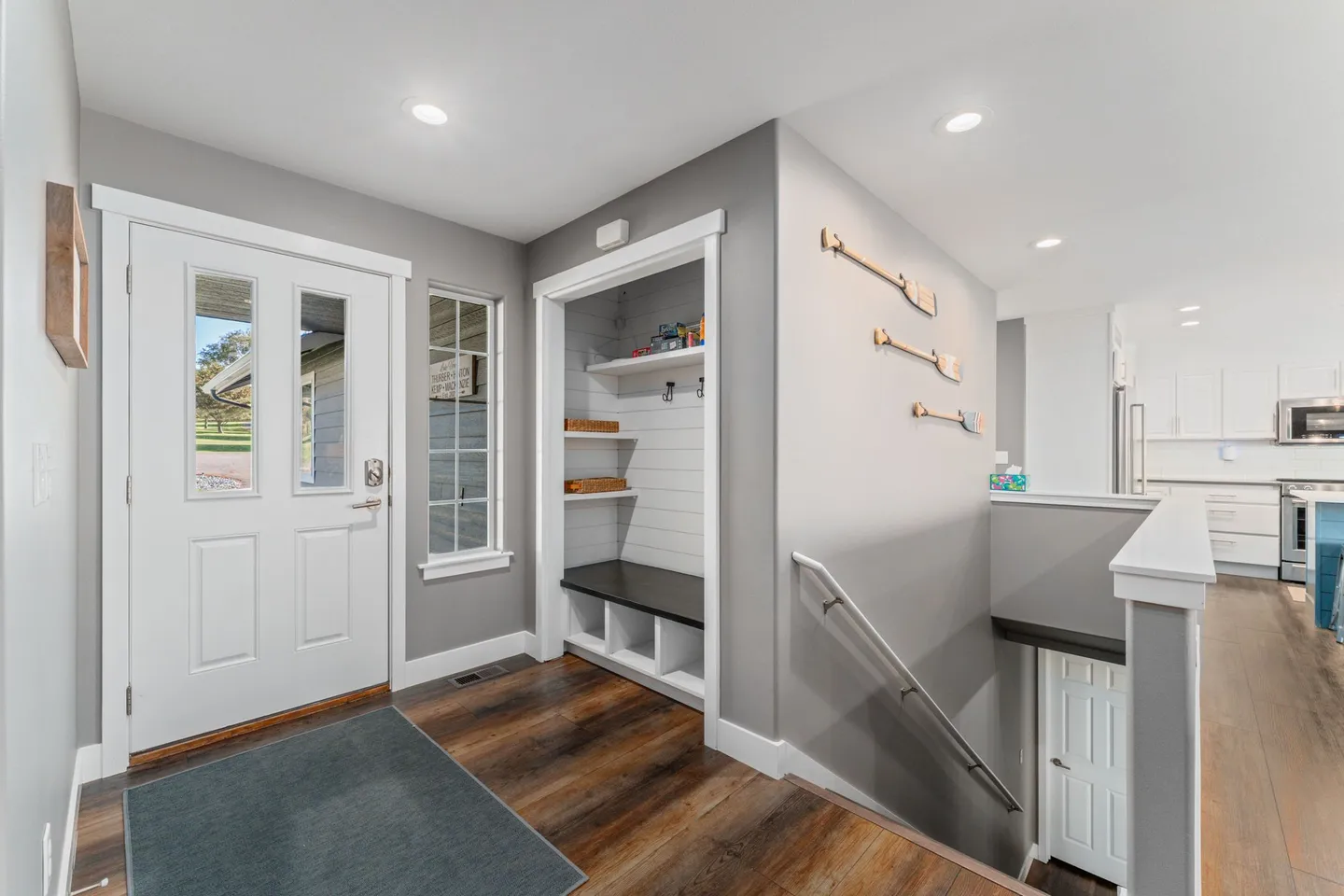 Entryway with a white front door, dark wood-look flooring, a built-in coat nook with a bench, and stairs leading down.