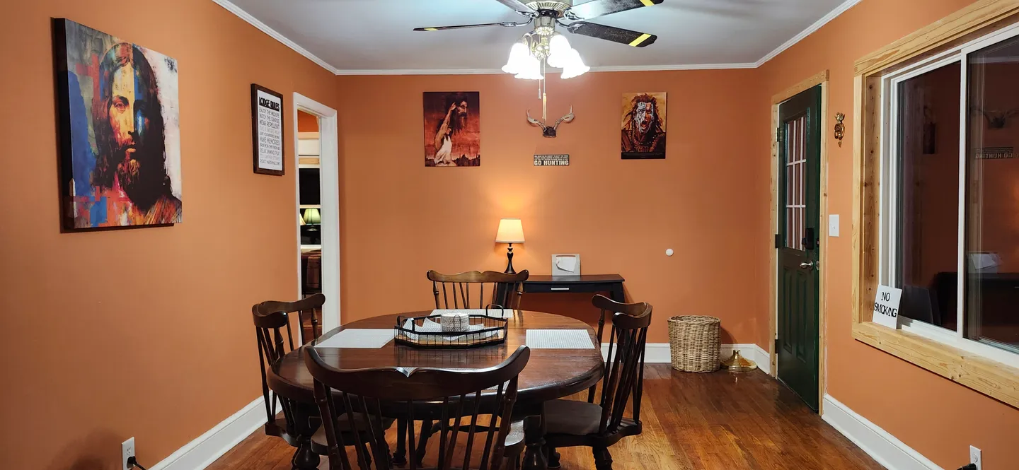 Dining room with terracotta orange walls, a round wooden dining table, and ceiling fan.