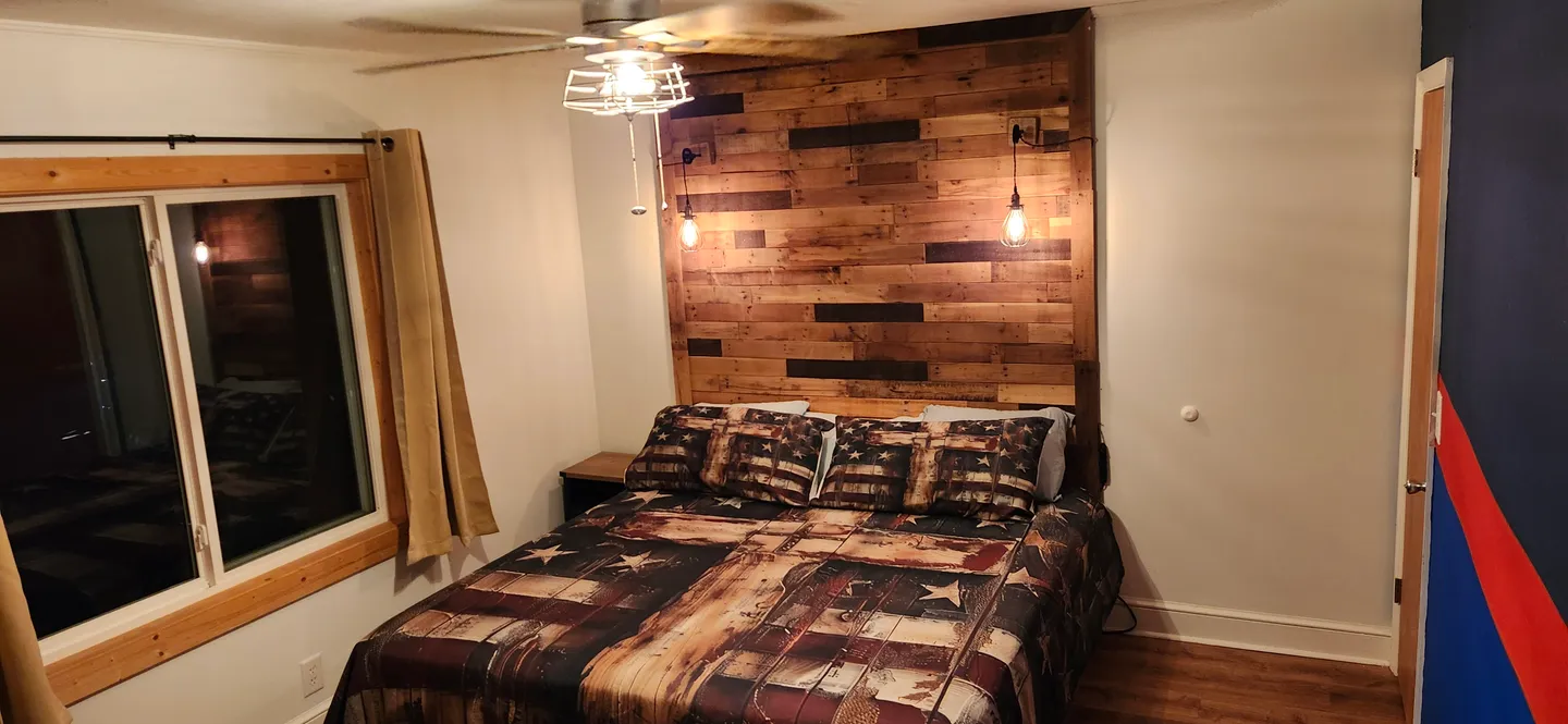 Bedroom featuring a bed with a rustic wood-plank headboard wall, matching patterned bedding, and pendant lights.