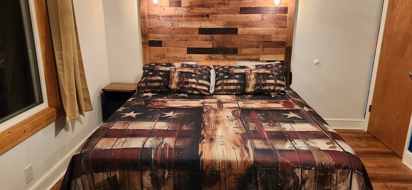 Bedroom featuring a bed with a rustic American flag-themed comforter and a wooden plank headboard.
