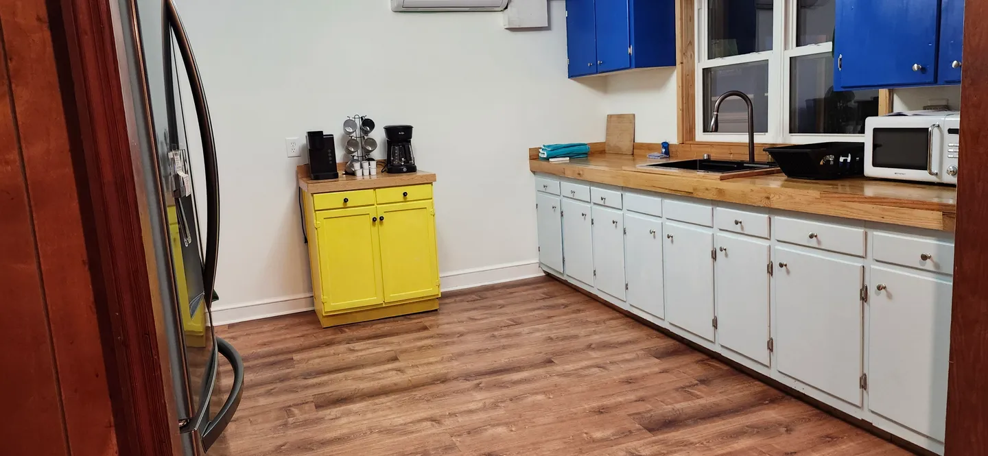 Kitchen with wood-style flooring, light-colored base cabinets, wood countertops, a yellow accent cabinet, and blue upper cabinets.