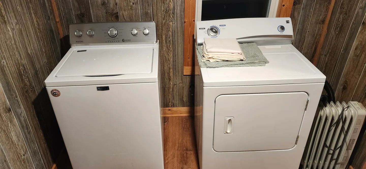 A white top-loading washing machine and white front-loading dryer set against wood-paneled walls.
