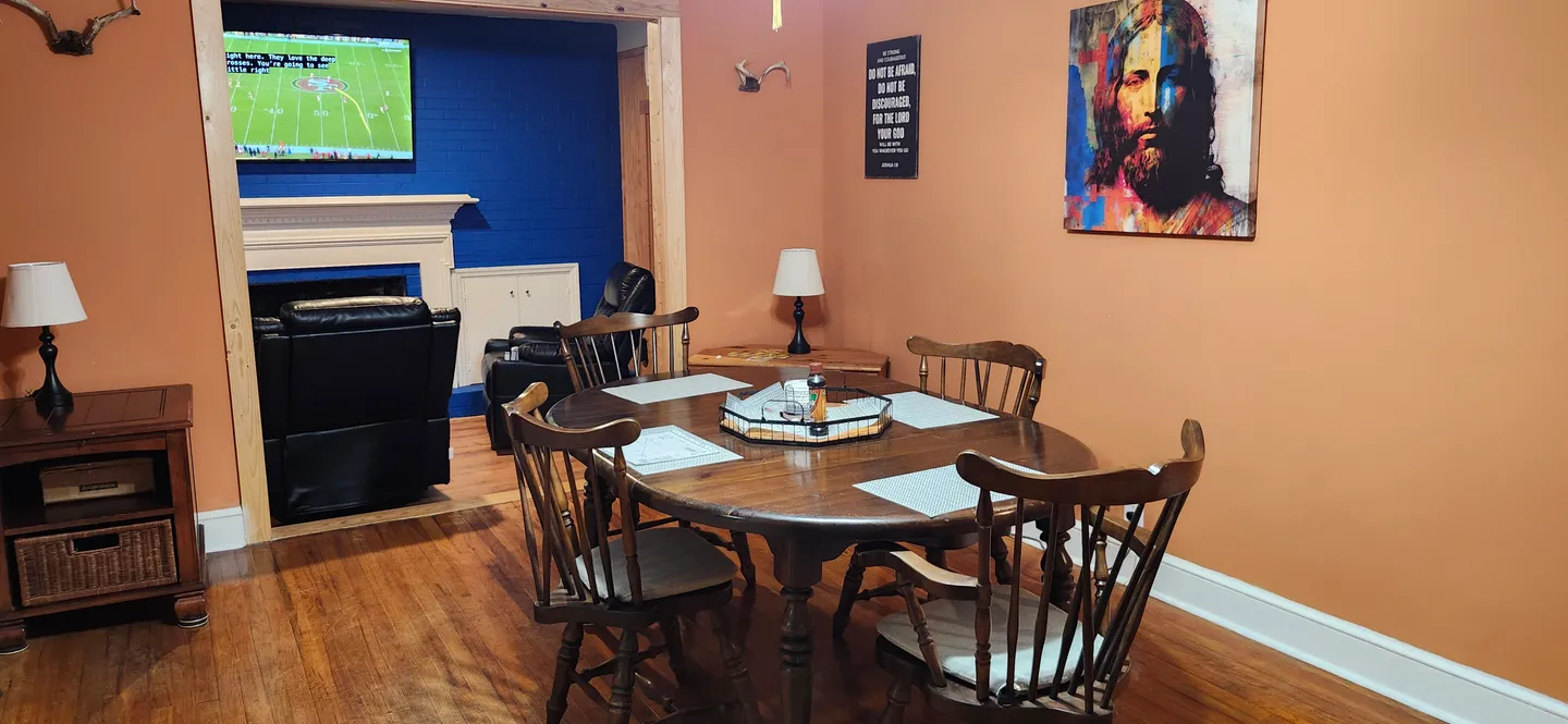 Dining area with an oval wooden table and chairs, adjacent to a living space with a fireplace and television.