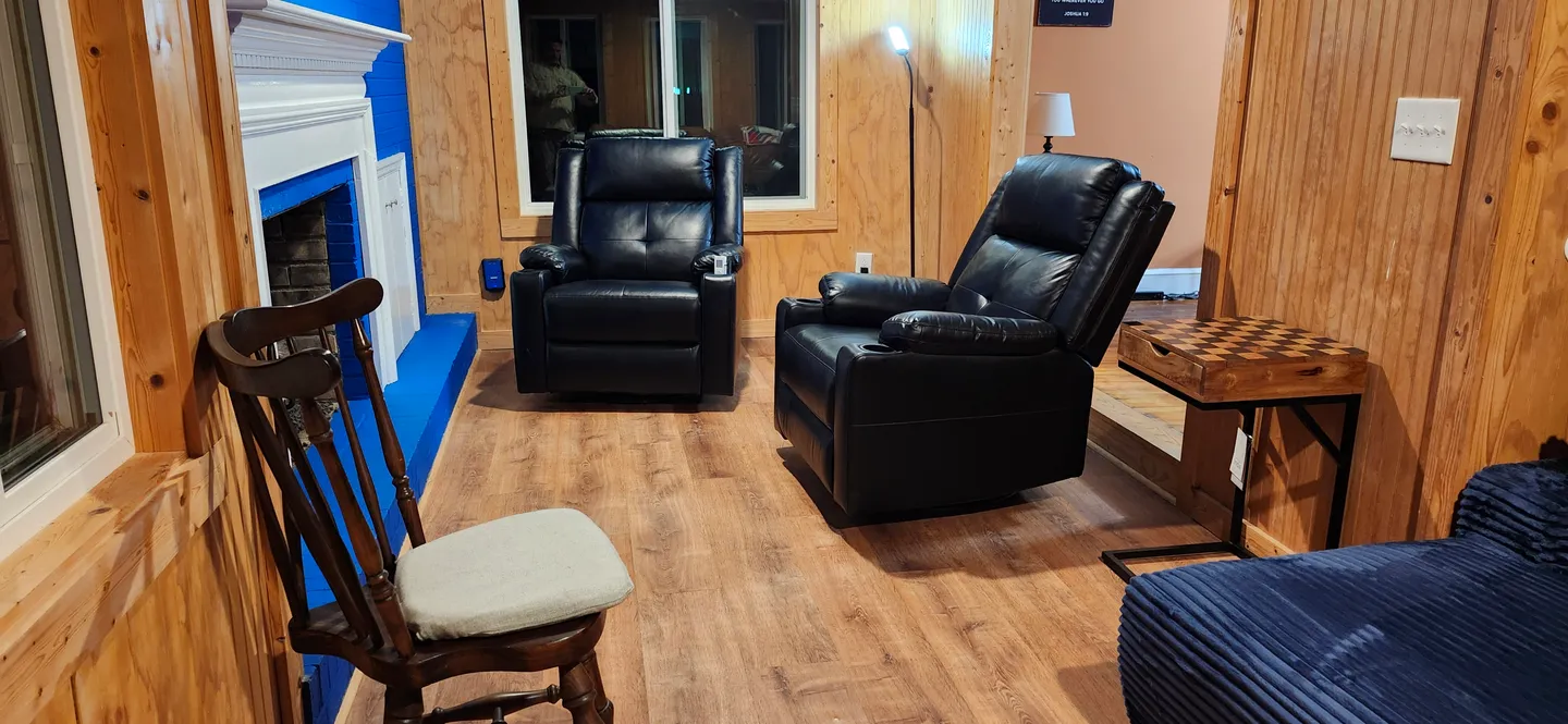 Living area featuring wood-paneled walls, two black leather recliners, a fireplace, and wood-look flooring.