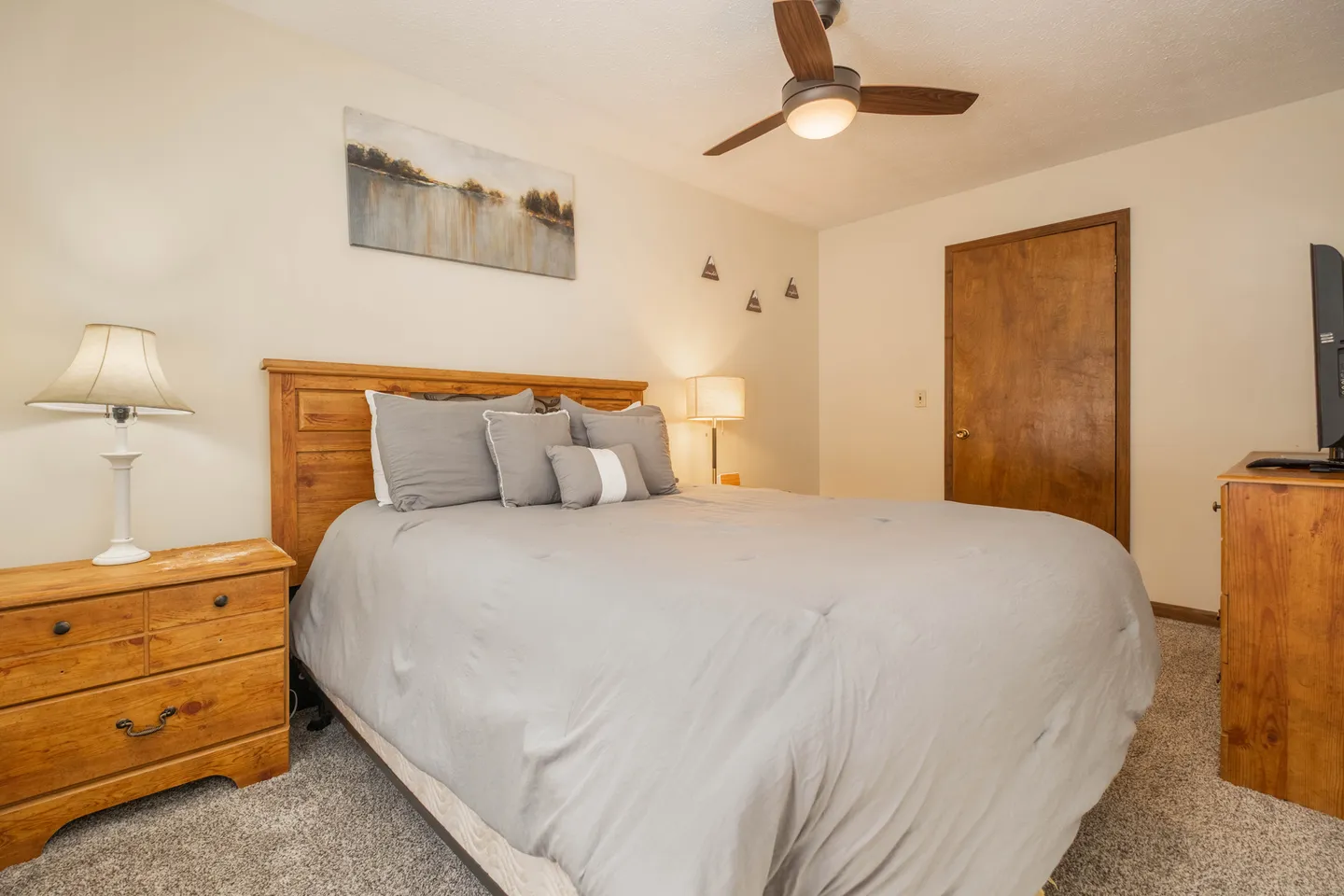 Bedroom featuring a made bed with gray bedding, wooden headboard, matching nightstand, and ceiling fan.