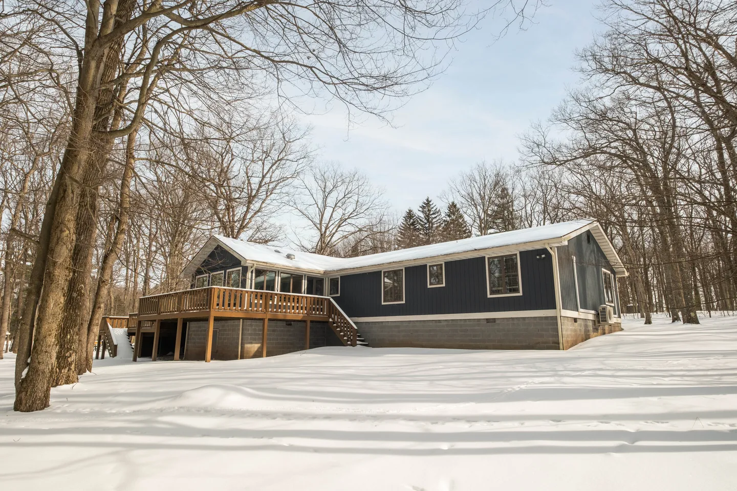 Exterior of a blue house with a raised wooden deck and snow-covered ground surrounded by bare winter trees.