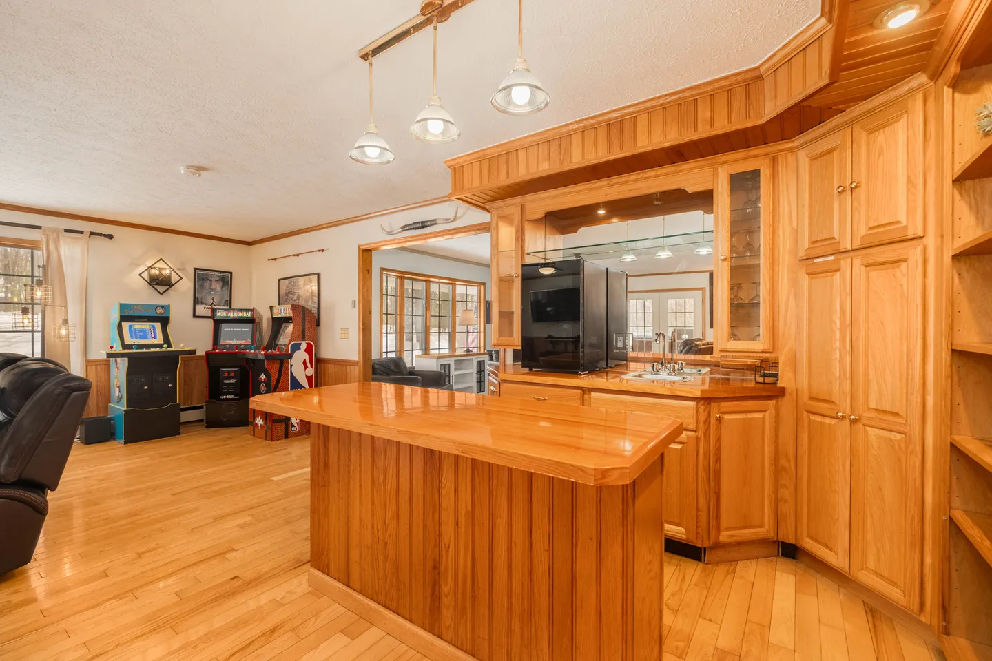Game room featuring wooden wet bar with island counter, mirrored backdrop, and arcade cabinets against the wall.