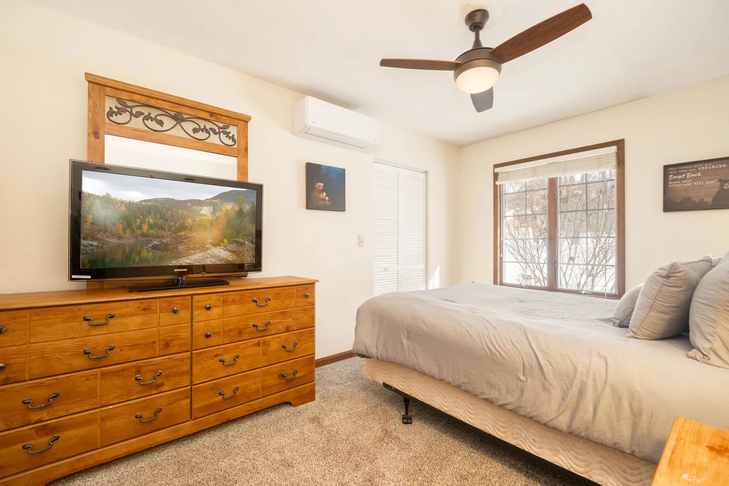 Bedroom with a bed, wooden dresser, television, ceiling fan, and wall-mounted air conditioning unit.