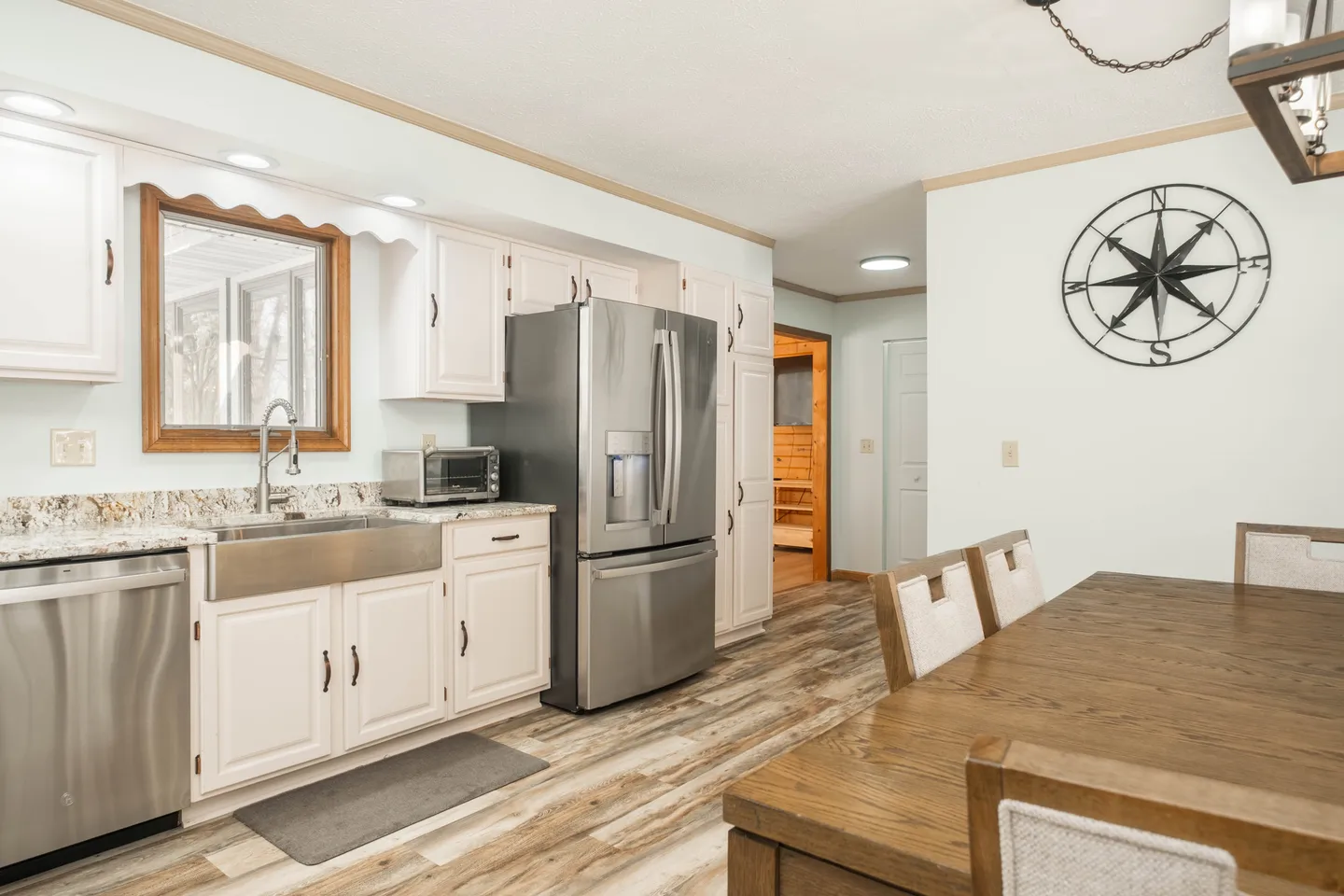 Kitchen with white cabinetry, stainless steel appliances, and a wood dining table in the foreground.