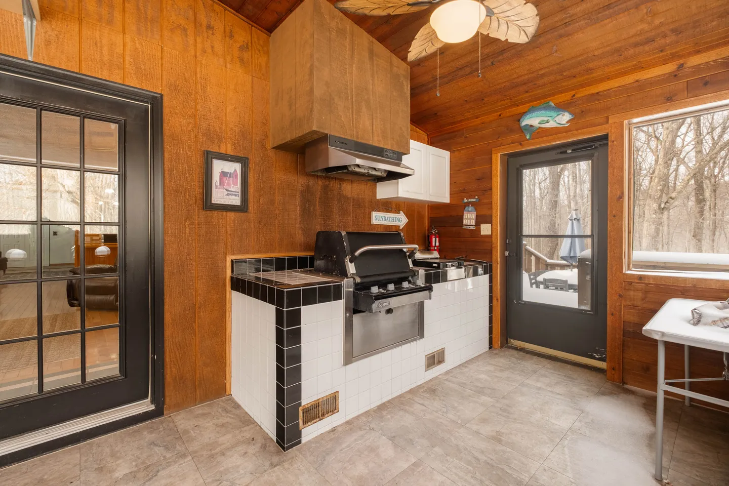 Enclosed porch or sunroom featuring wood-paneled walls and an indoor cooking station with a built-in grill, vent hood, and tiled counter.