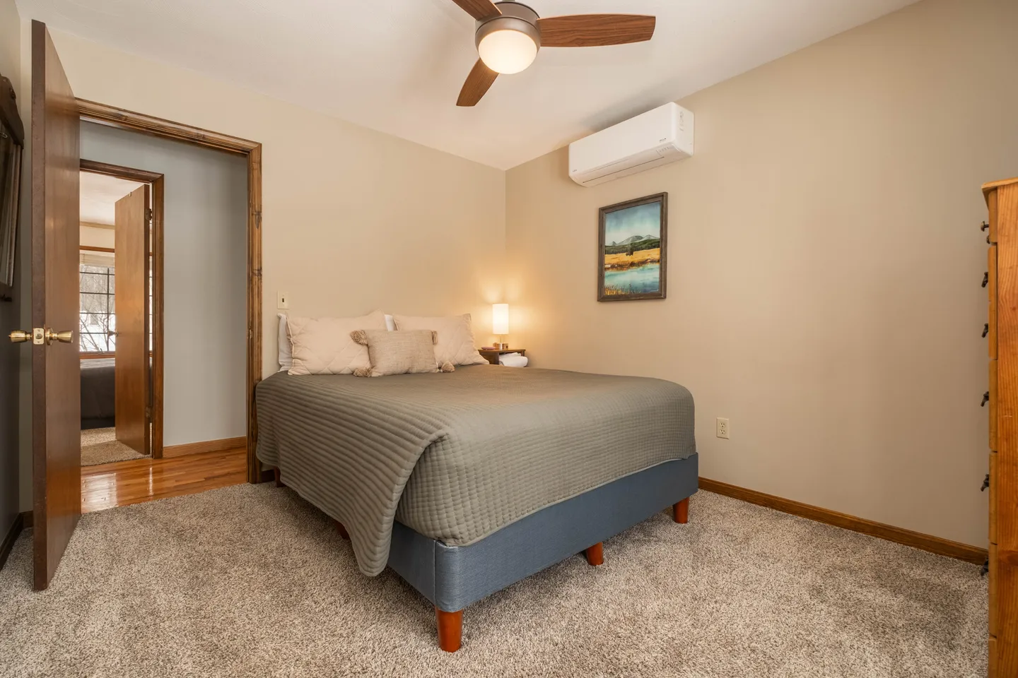 Bedroom featuring a made bed with a green coverlet, carpeted floor, ceiling fan, and wall-mounted air conditioning unit.