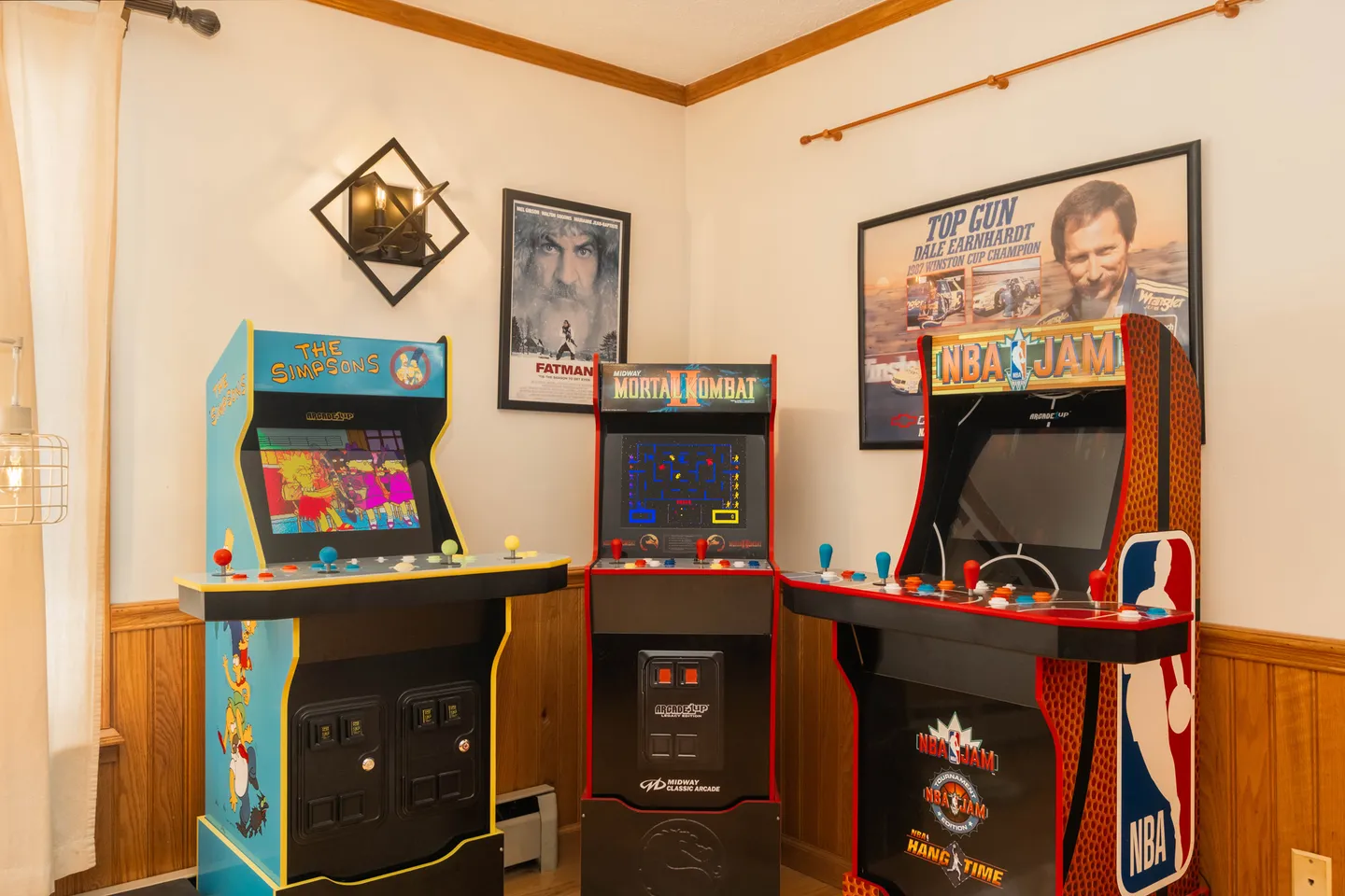 Three classic arcade game cabinets lined up against the wall in a room with framed posters.