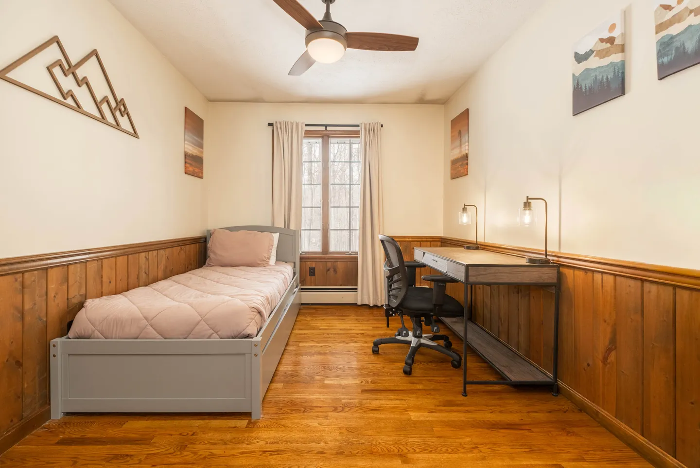 Bedroom featuring wood floors, wainscoting, a single bed, and a desk with an office chair below a ceiling fan.
