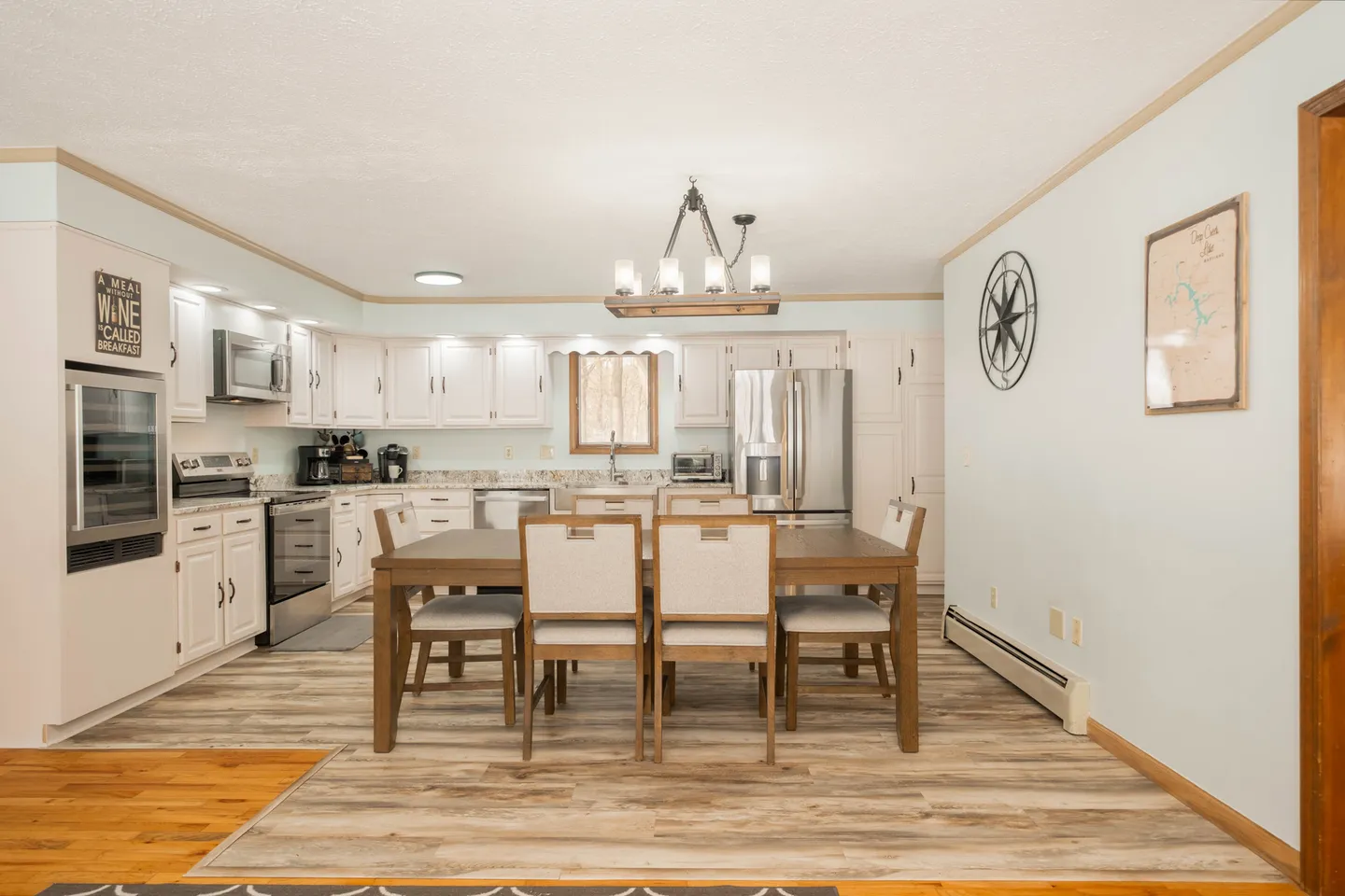 Dining area with a wooden table and chairs in front of a white kitchen with stainless steel appliances.