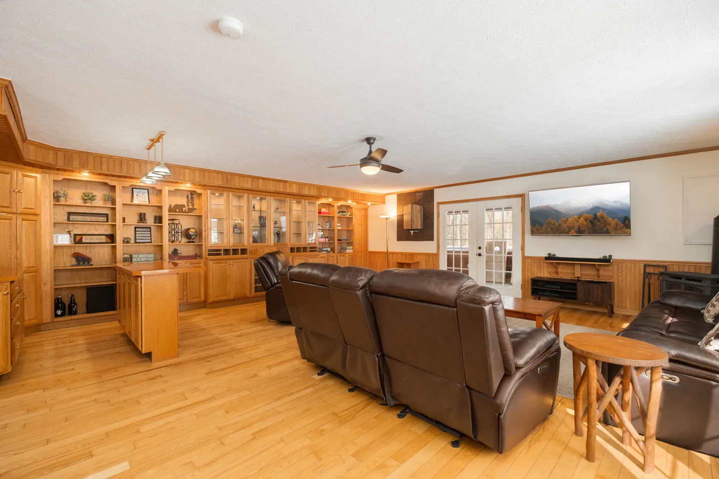 Spacious living room featuring wood floors, custom built-in wooden cabinetry, leather reclining sofas, and a wall-mounted TV.