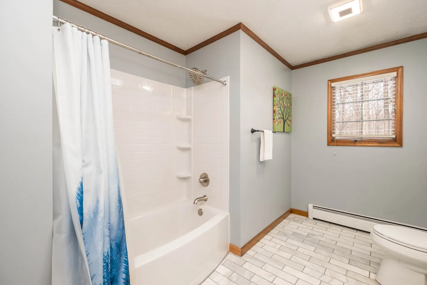 Bathroom with a white bathtub and shower combination, tiled floor, toilet, and window with blinds.