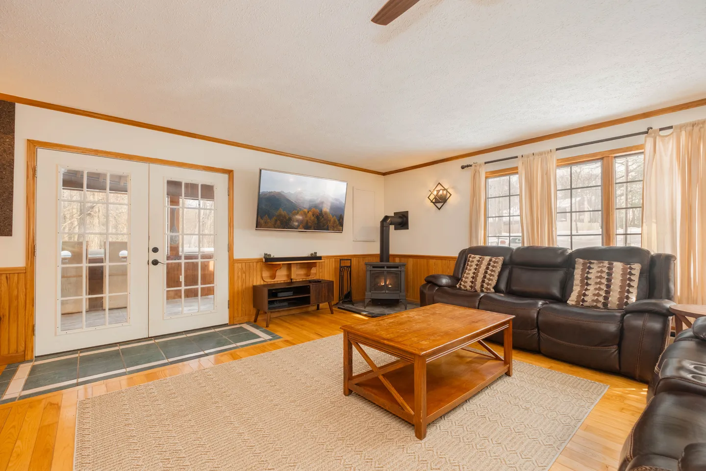 Living room with leather sofa, wood coffee table, wall-mounted television, wood-burning stove, and glass patio doors.