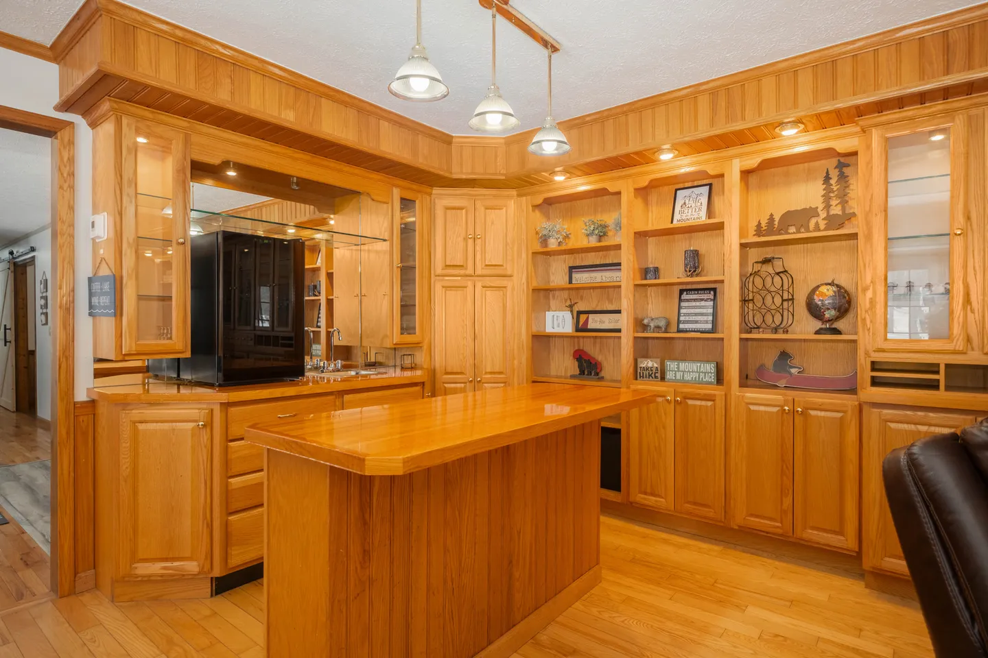 Built-in wooden wet bar and entertainment cabinetry with an island counter, overhead pendant lights, and integrated shelving.