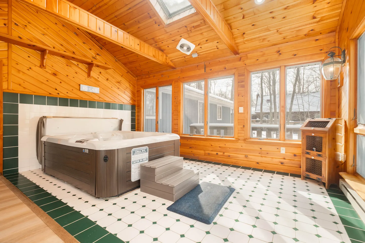 Indoor hot tub room with wooden walls and ceiling, tiled floor, skylight, and large windows.