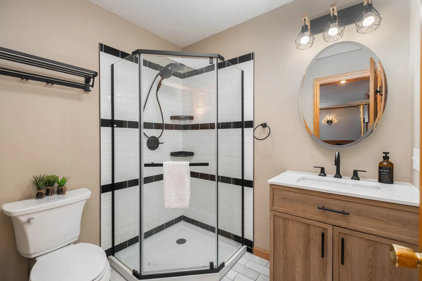 Bathroom with a corner glass shower, white toilet, round mirror, and wood-finish vanity with black hardware.