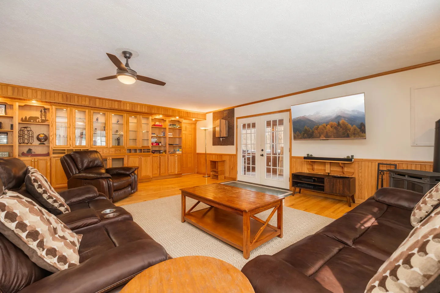 Living room with brown leather sofas, coffee table, wall-mounted TV, and extensive wooden built-in cabinetry.
