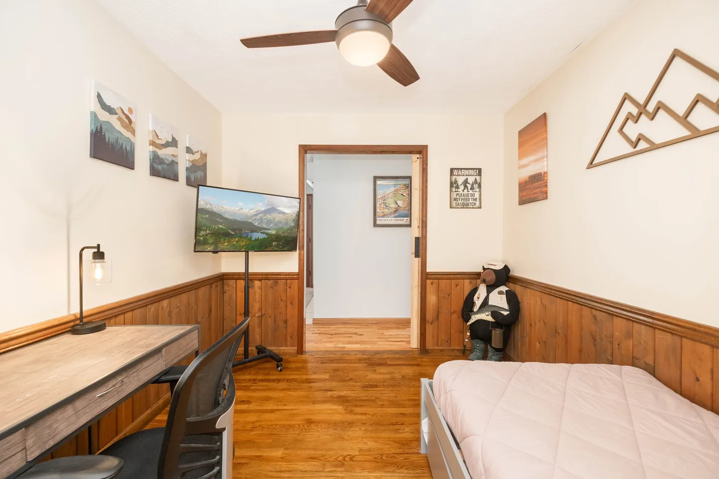 Bedroom featuring wood wainscoting, hardwood floors, a desk with chair, a single bed, and a mounted flat-screen TV.