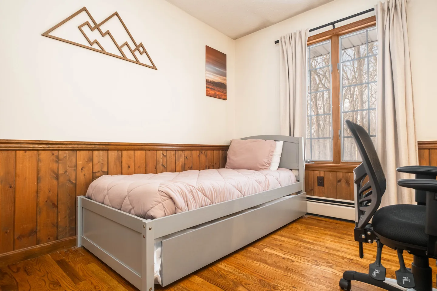 Bedroom corner with a gray daybed, wooden wainscoting, hardwood floors, an office chair, and a window.