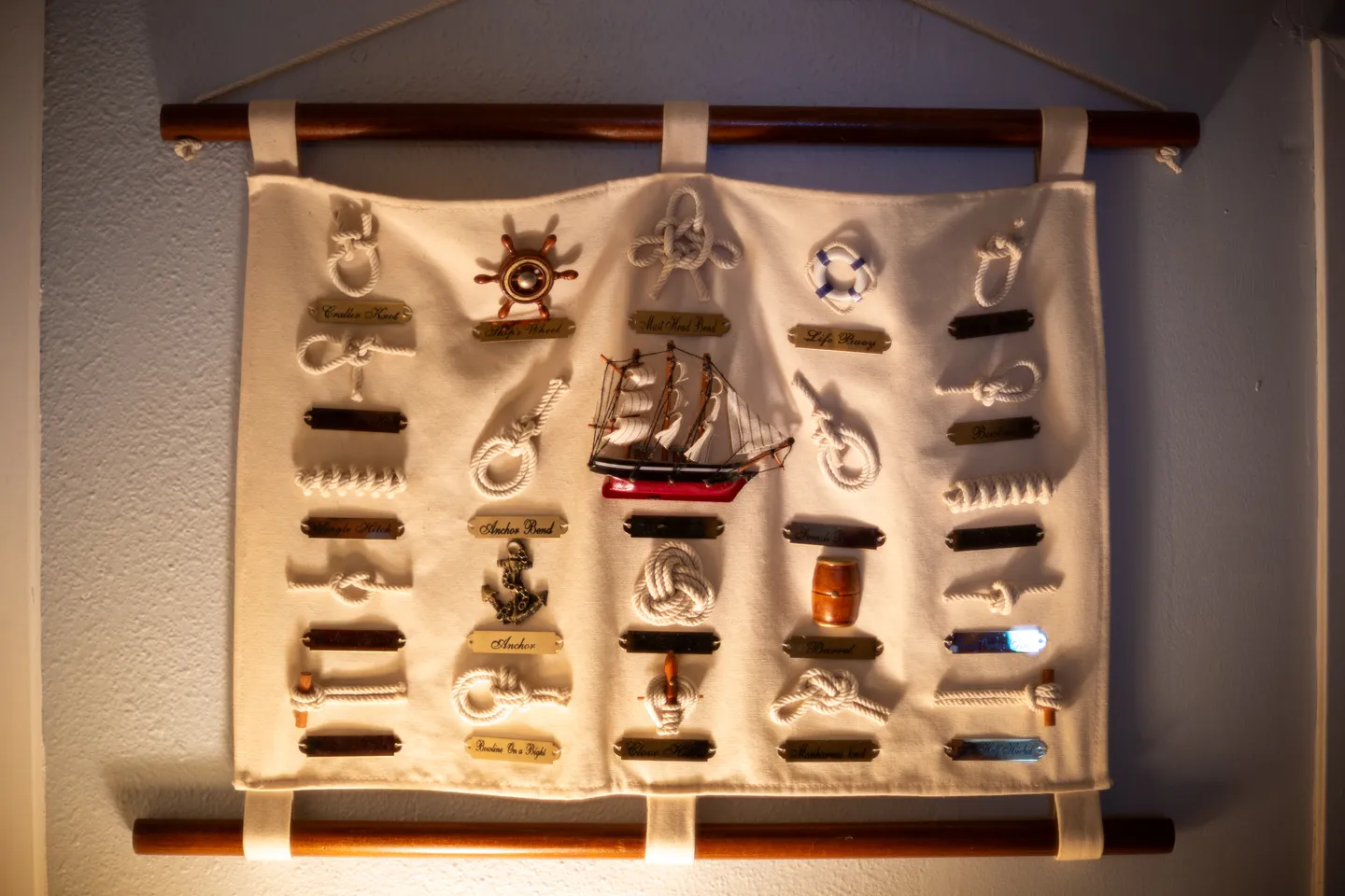 Nautical knot and miniature ship display hanging on a light-colored wall.