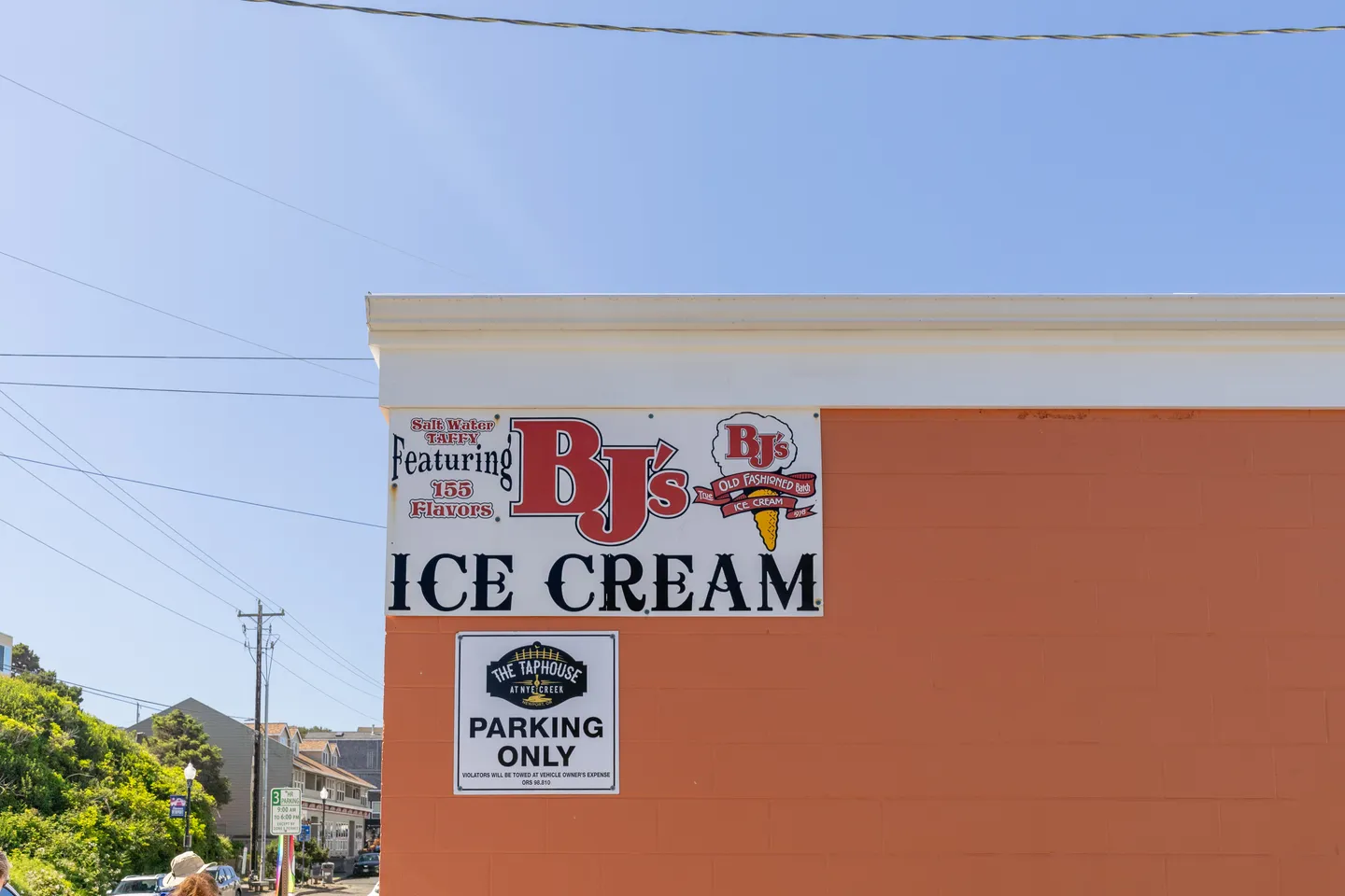 Exterior corner of a building with signage for BJ's Ice Cream and parking restrictions under a clear blue sky.