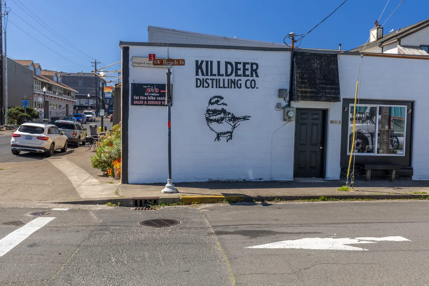 Exterior view of Killdeer Distilling Co. building on a sunny street corner near the coast.