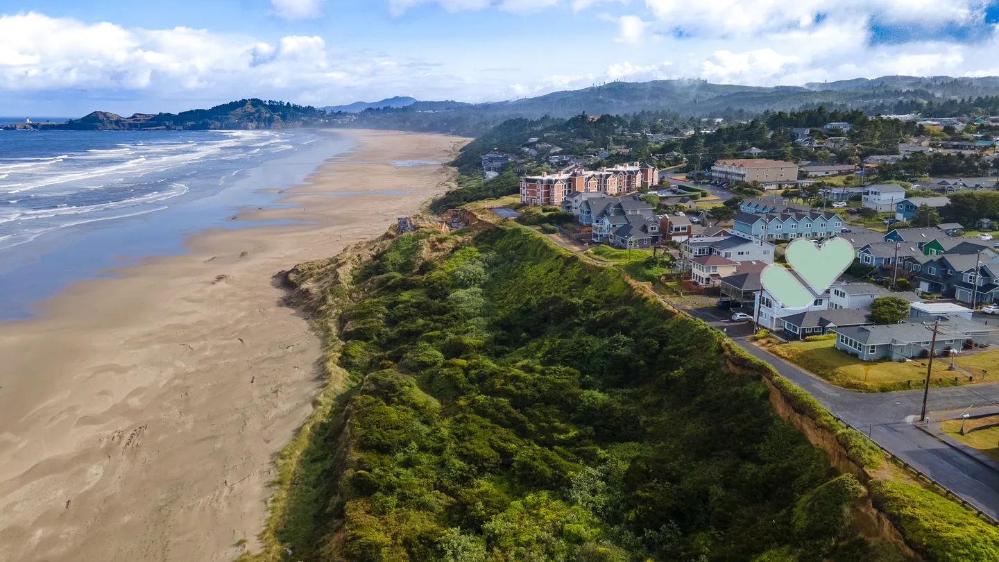 Aerial view of a coastal neighborhood situated on a bluff directly overlooking an expansive sandy beach and ocean waves.