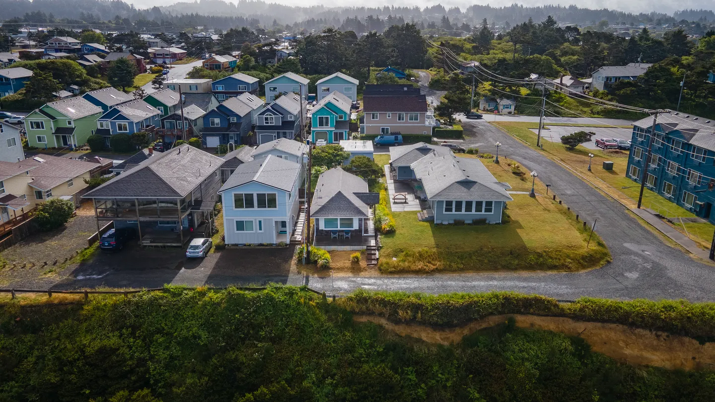 Aerial view of a coastal neighborhood with single-family houses near a cliffside road.