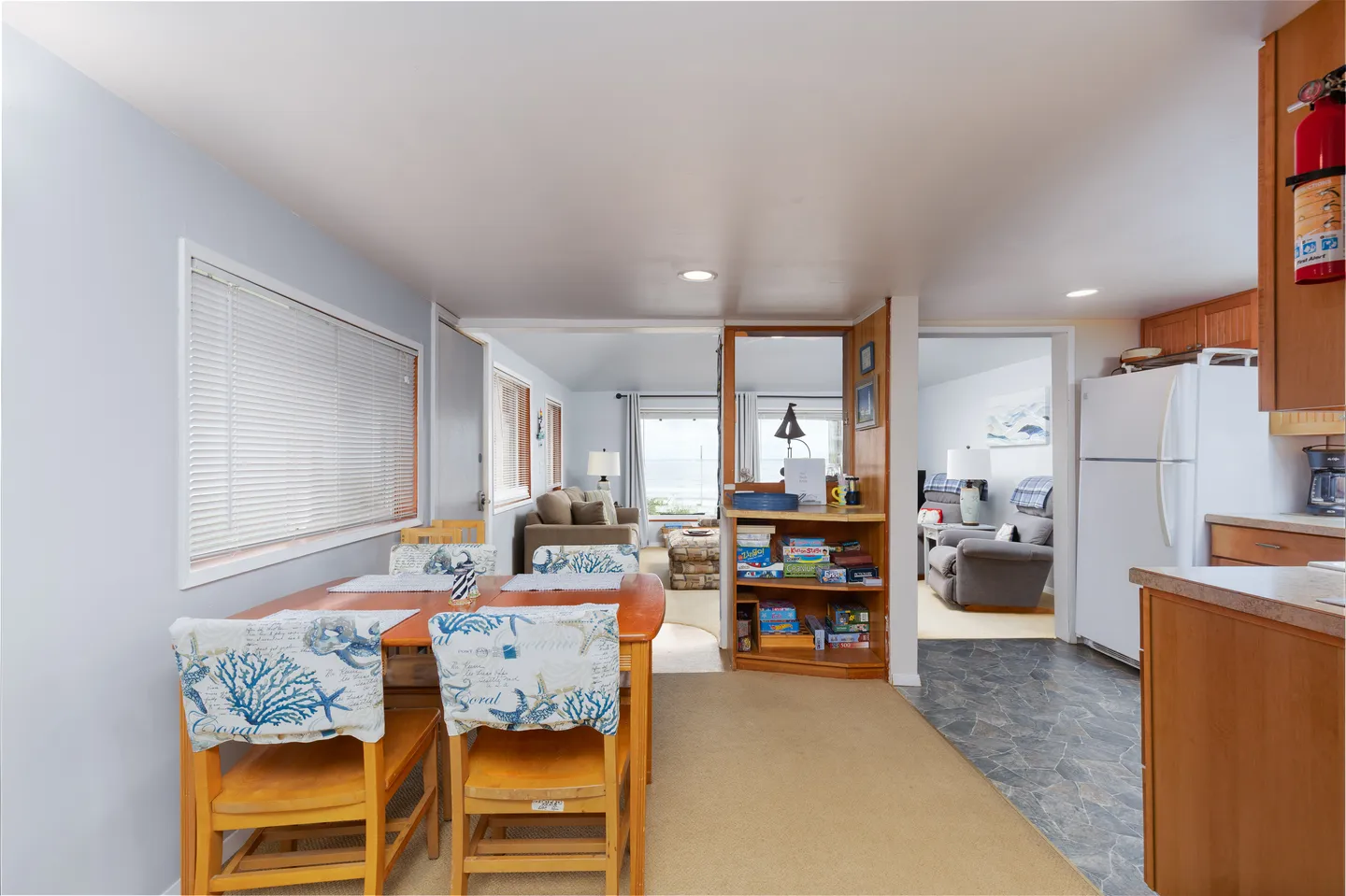 Dining area with a wooden table and patterned chairs, adjacent to a kitchen and opening into a living room.