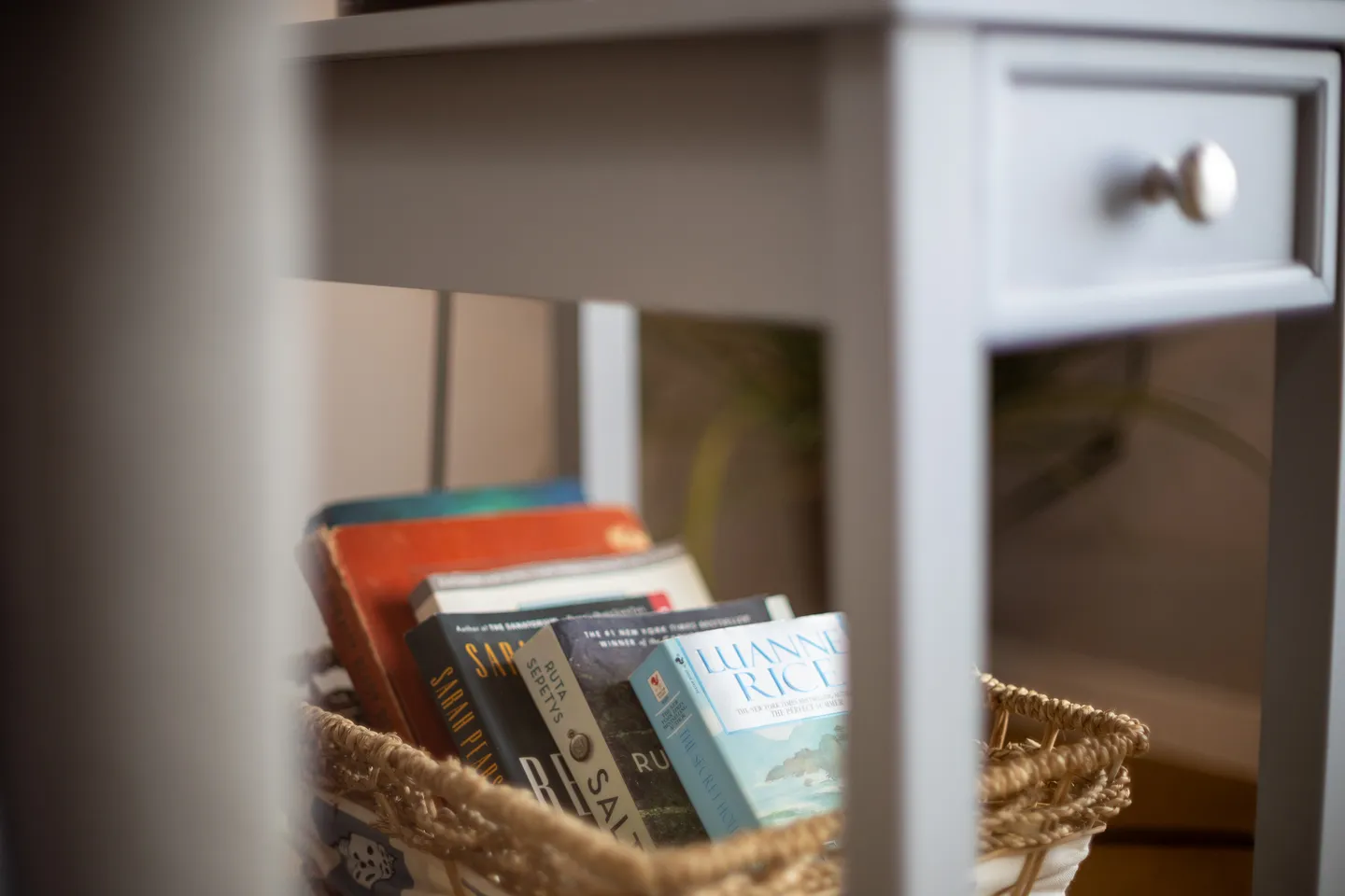Close-up of a woven basket filled with books placed under a light-colored side table.
