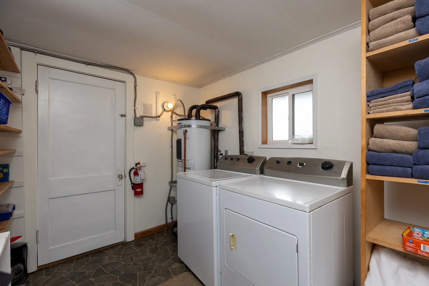 Laundry room with white washer and dryer, water heater, towel shelving, and an exterior door.
