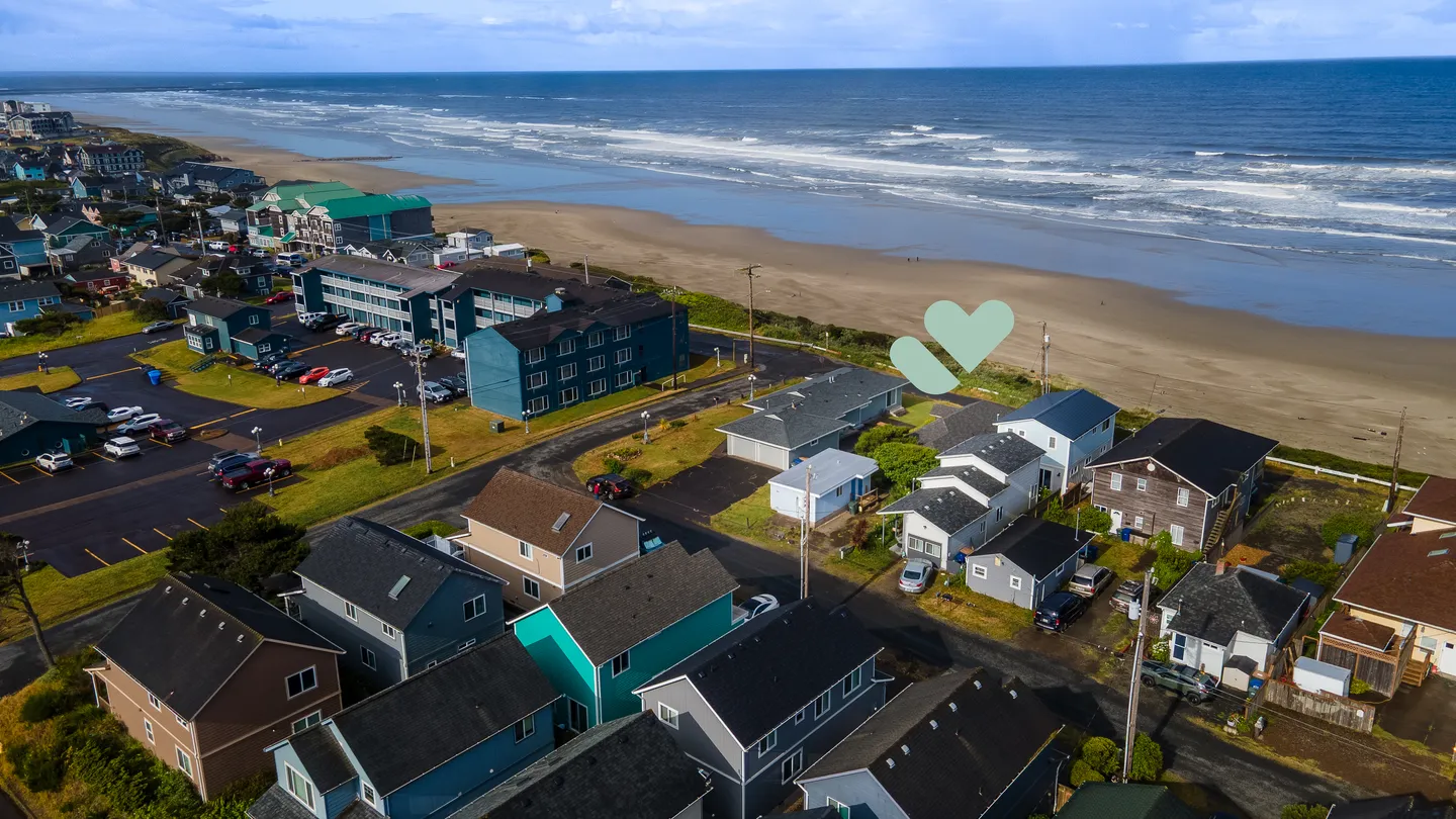 High-angle aerial view of coastal houses and residential buildings along an ocean beach with breaking waves.