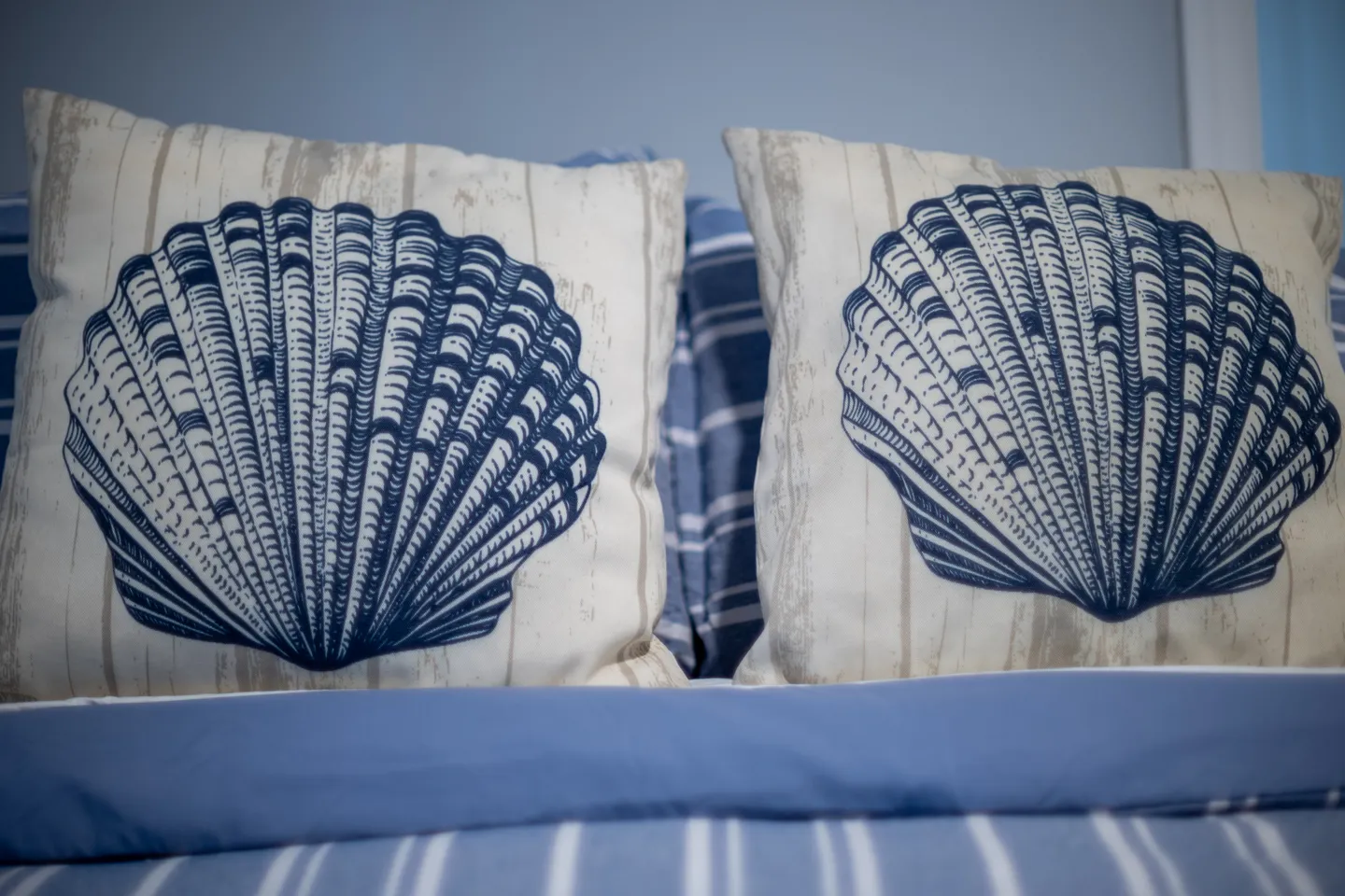 Close-up of decorative throw pillows featuring navy blue seashell prints on a bed.