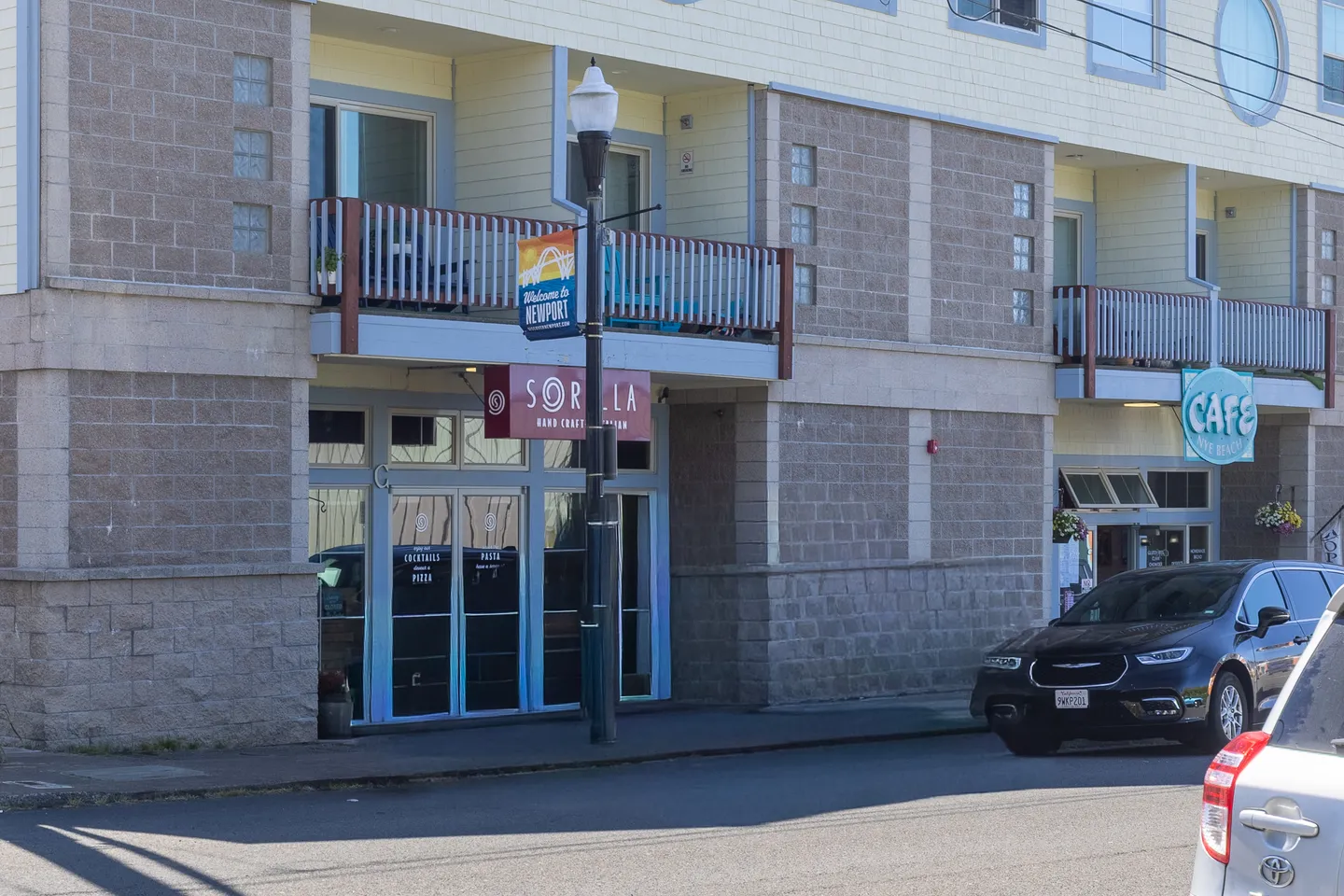 Exterior view of a multi-story building featuring ground-floor storefronts and upper-level balconies along a street.