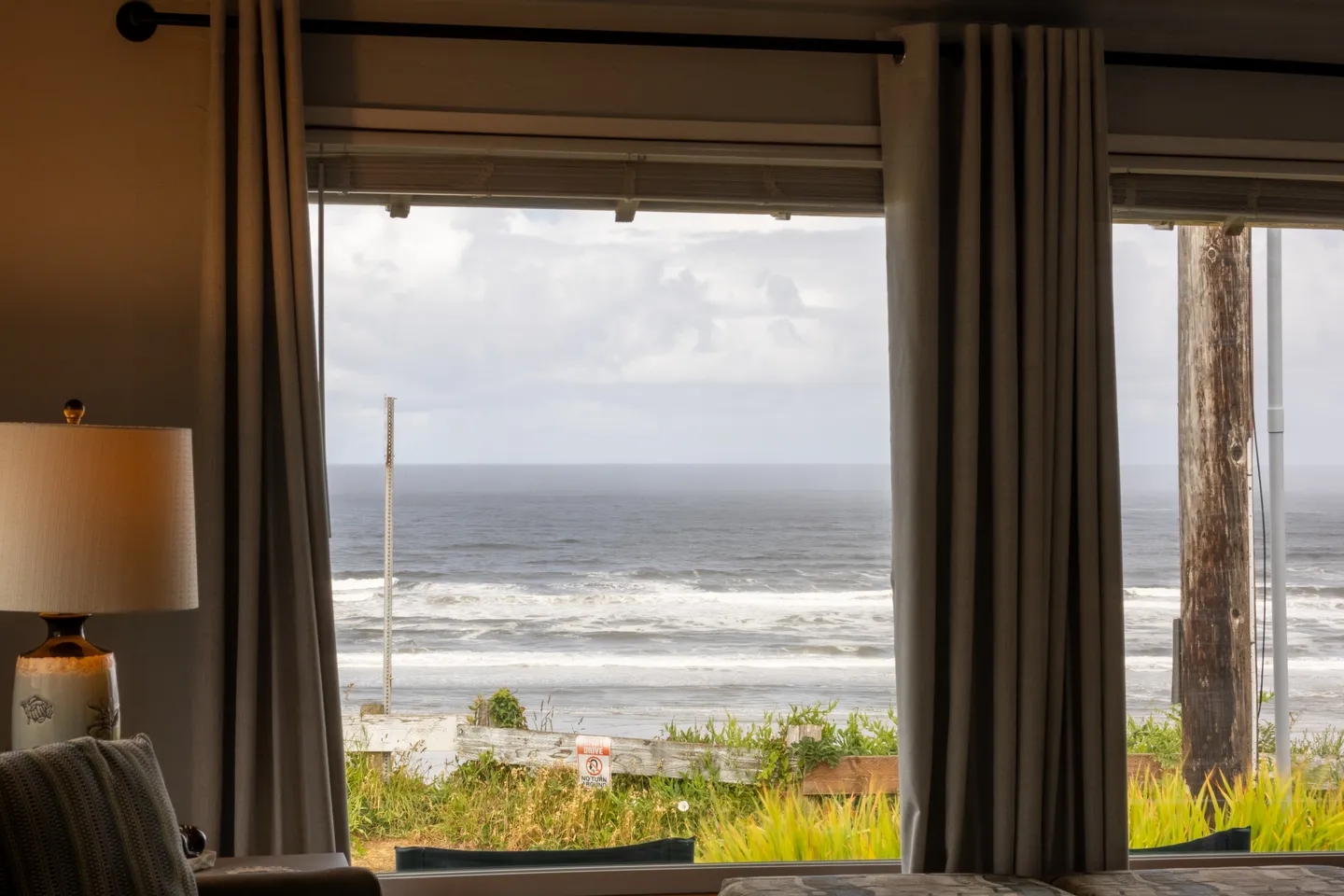 View of the ocean with rolling waves seen through a large window framed by neutral curtains.