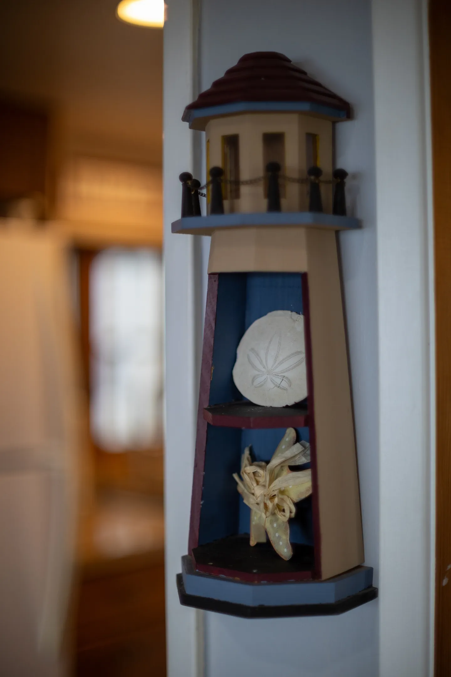 Close-up of a decorative lighthouse wall hanging holding a sand dollar and dried sea star.