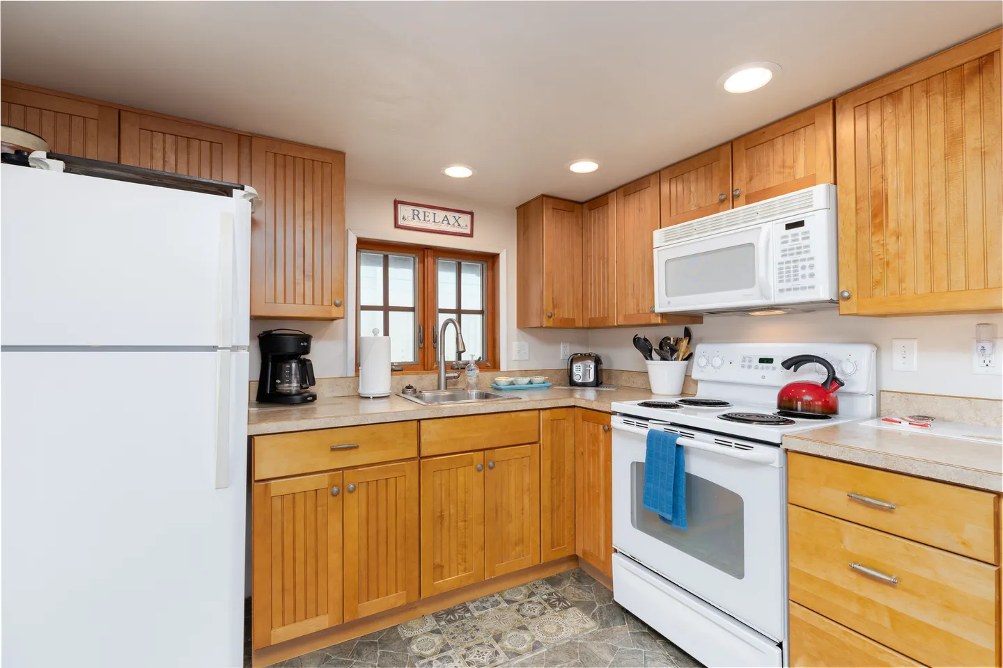 Compact kitchen corner featuring wood paneled cabinets, white appliances, and a window above the sink.