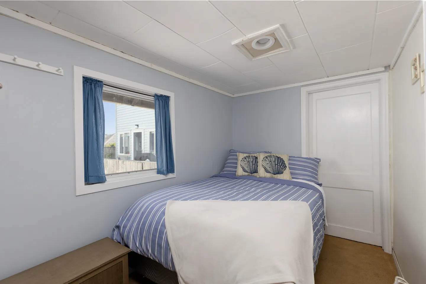 Bedroom with blue striped bedding, a window with blue curtains, and light blue walls.