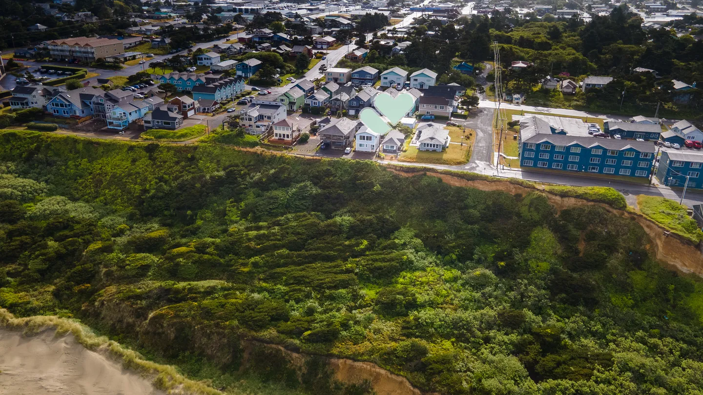 Aerial view of a coastal neighborhood situated on a bluff with dense greenery above a sandy beach area below.