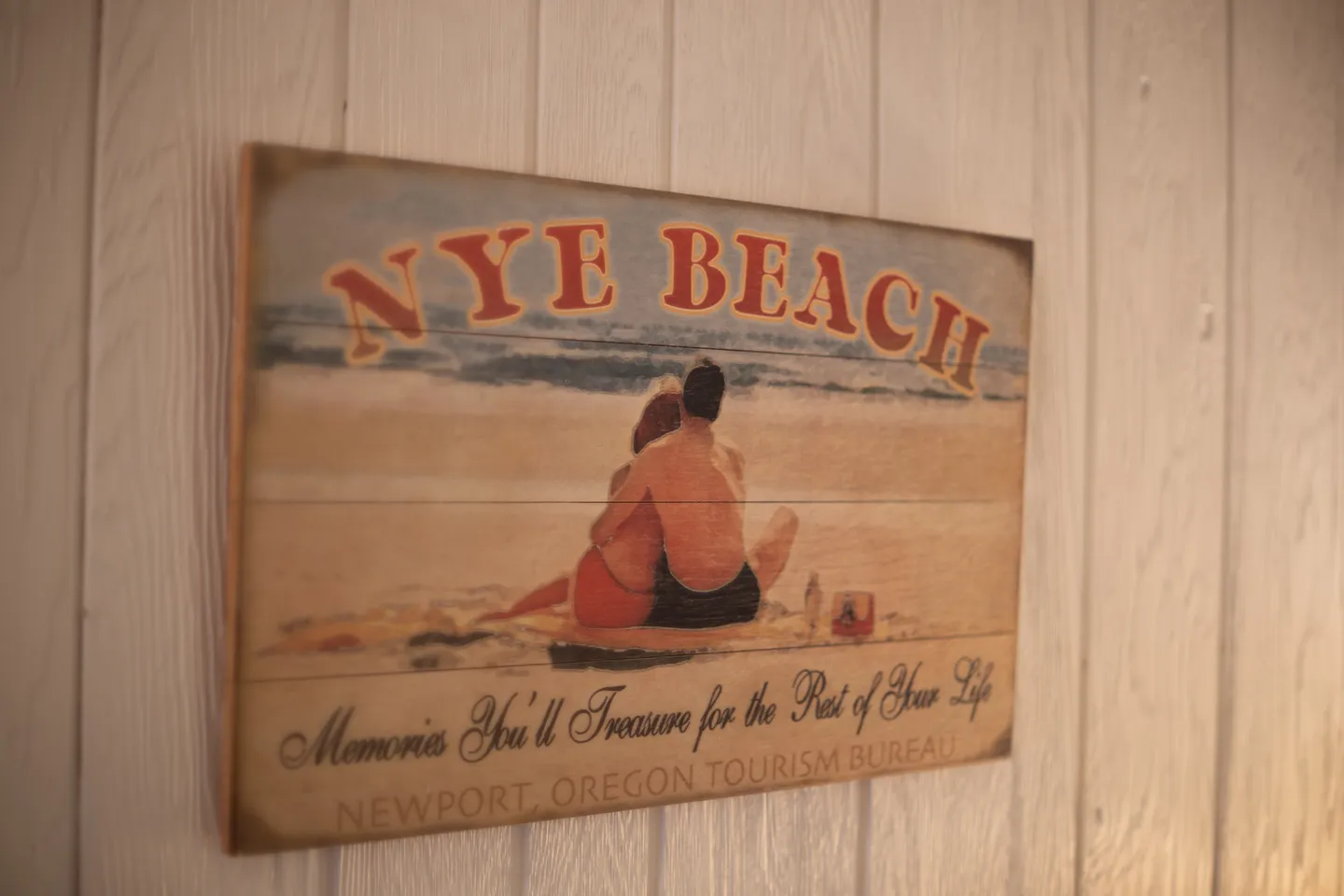 A vintage-style Nye Beach decorative wall sign mounted on light-colored wood paneling.